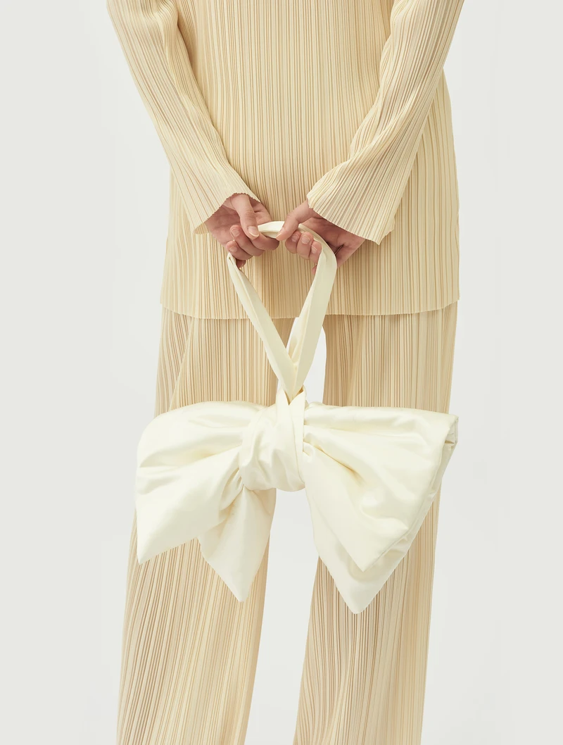 Ivory bow bag held with a cream pleated outfit